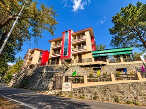 A multi-story building with balconies, a stone retaining wall, and a clear sky. - Hill View Homes (Nainital)