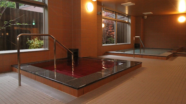 Un área de piscina interior moderna con paredes de vidrio transparente, un jacuzzi central y suelo de baldosas.