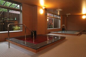 Un espace piscine intérieur moderne, doté de parois en verre transparent, d’un grand jacuzzi central et d’un sol carrelé.