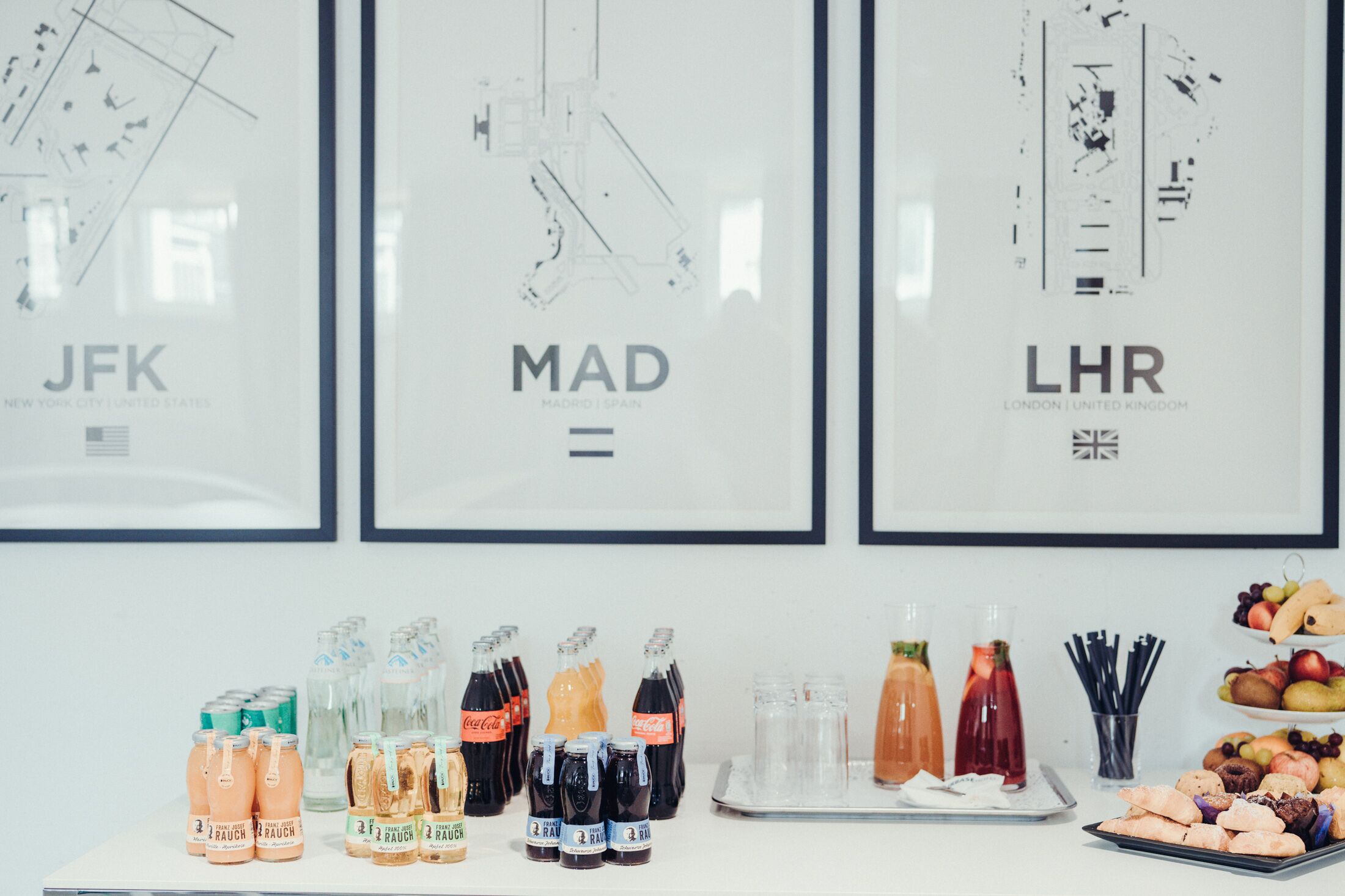 A table with various beverages and snacks, framed cityscape posters, and a tray of pastries.