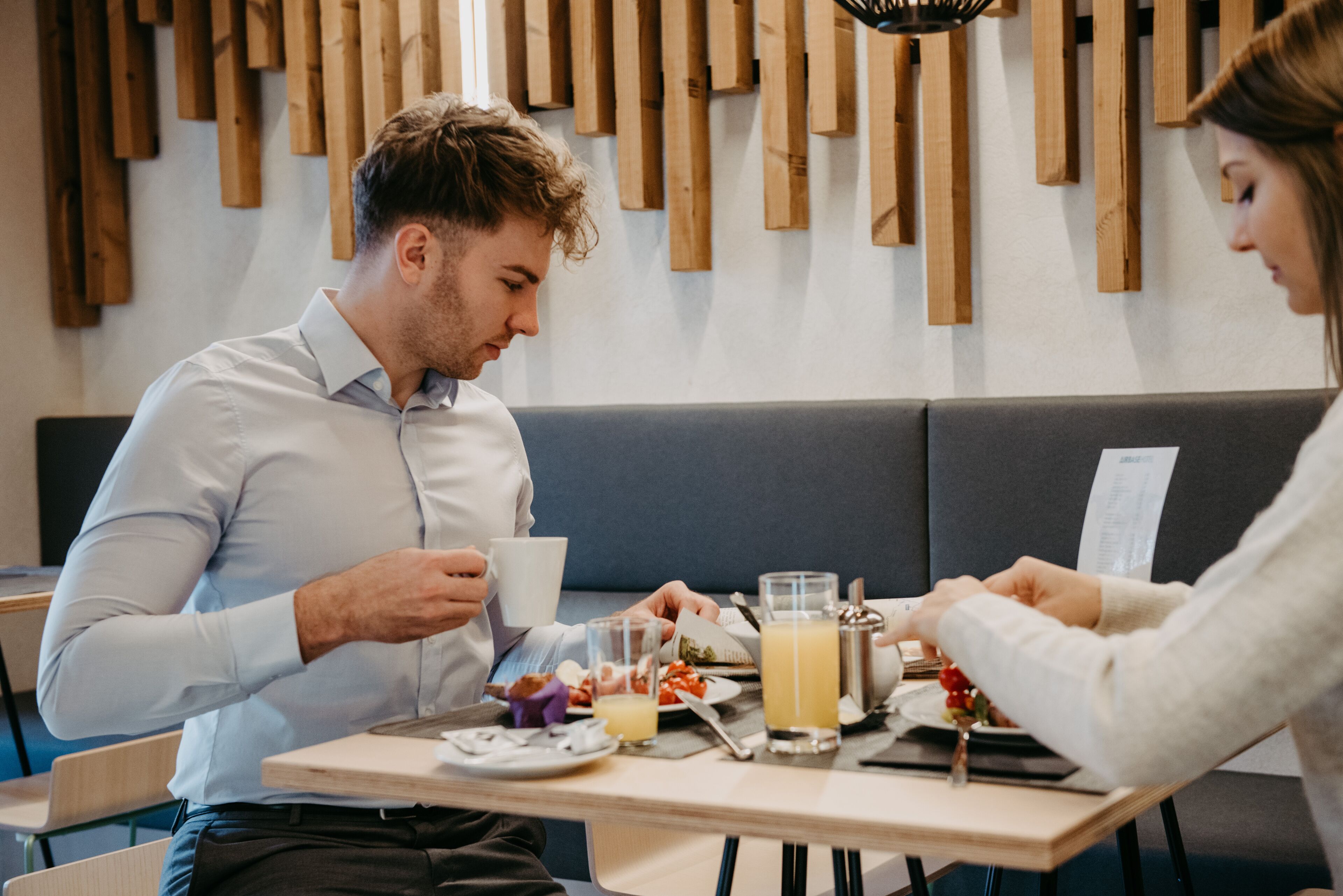 Een eetgedeelte met een houten wand, een grijze bank en een tafel gedekt met borden, glazen en een koffiepot.