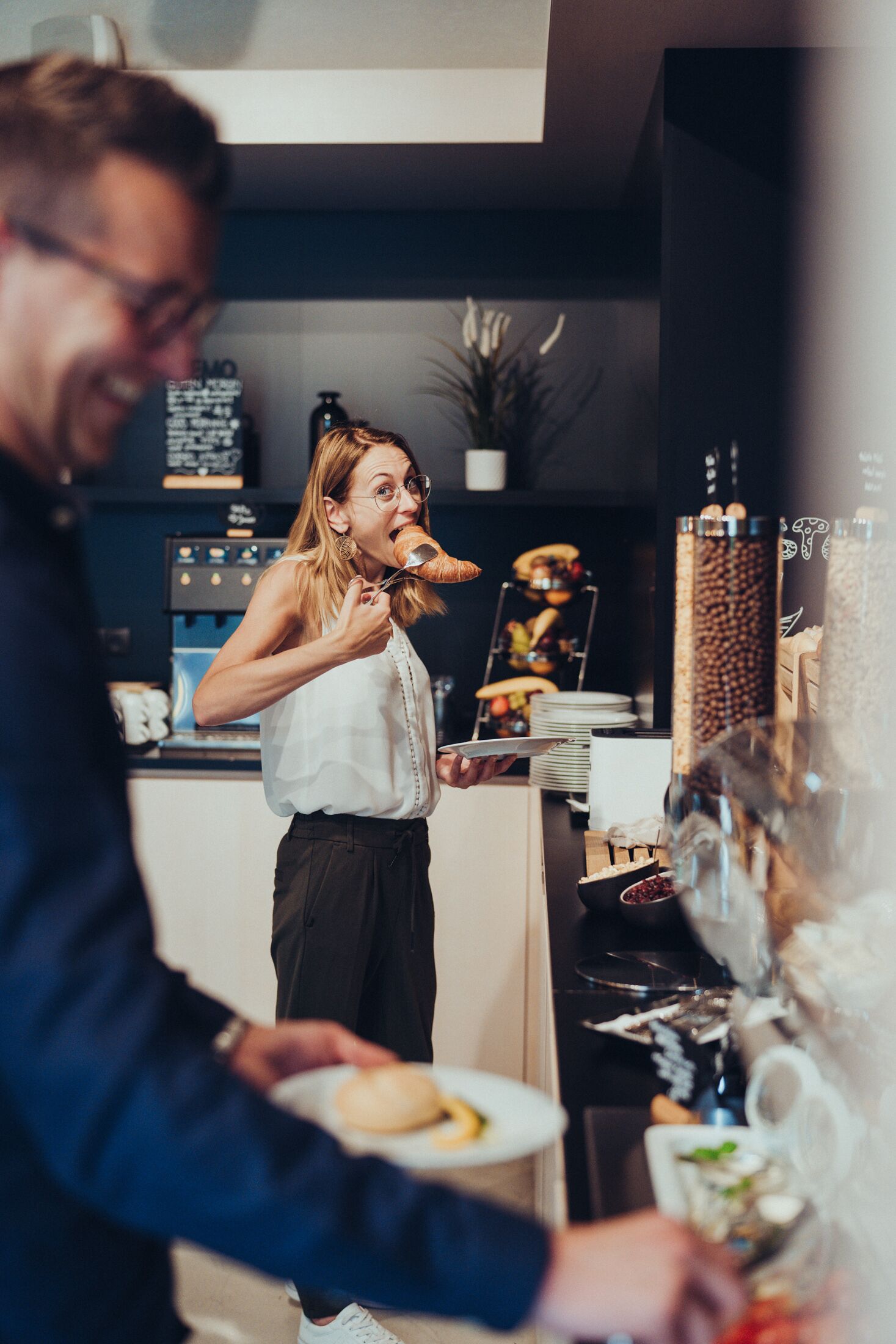 Una persona sirve comida en un café moderno, con una máquina de café y diversos alimentos al fondo.