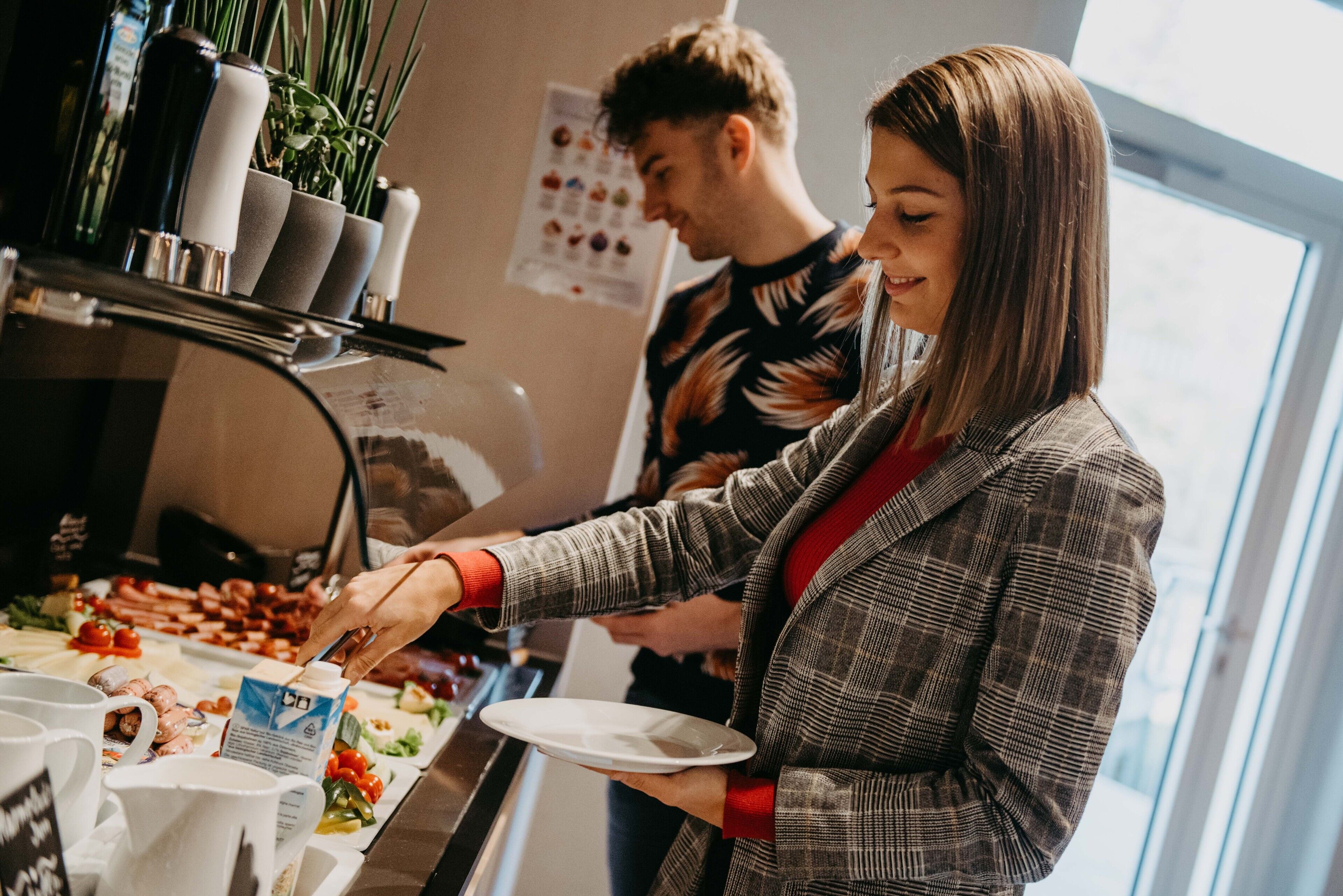 A buffet setup with various food items and a person serving themselves.