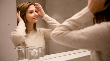 A person in a bathroom with a mirror, a sink, and a countertop with glasses.