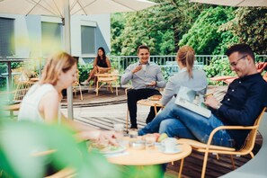 An outdoor patio with wooden tables and chairs, surrounded by greenery. - Airbase Hotel (Kalsdorf bei Graz)