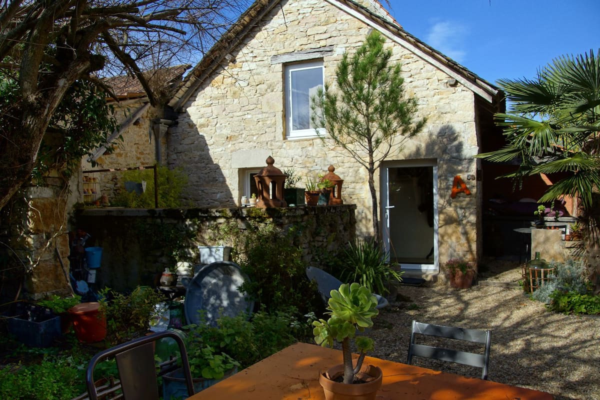 Une maison en pierre avec un petit jardin, une table en bois et une chaise.