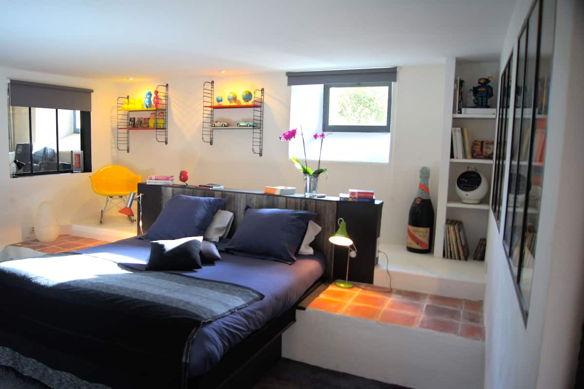 Une chambre à coucher moderne avec un lit, des tables de chevet, une lampe, une fenêtre et une bibliothèque.