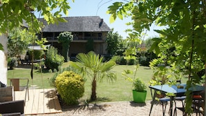 A two-story house with a balcony, surrounded by a well-maintained garden with various plants and a patio area with outdoor furniture.
