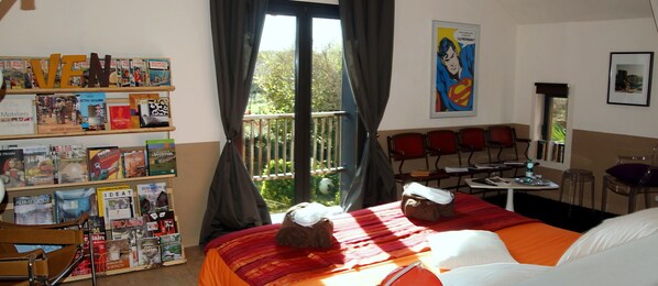 A hotel room with a large bed, a bookshelf with books, a balcony with a view, and a Superman poster on the wall. - La Maison de Louna (Salles-Courbaties)