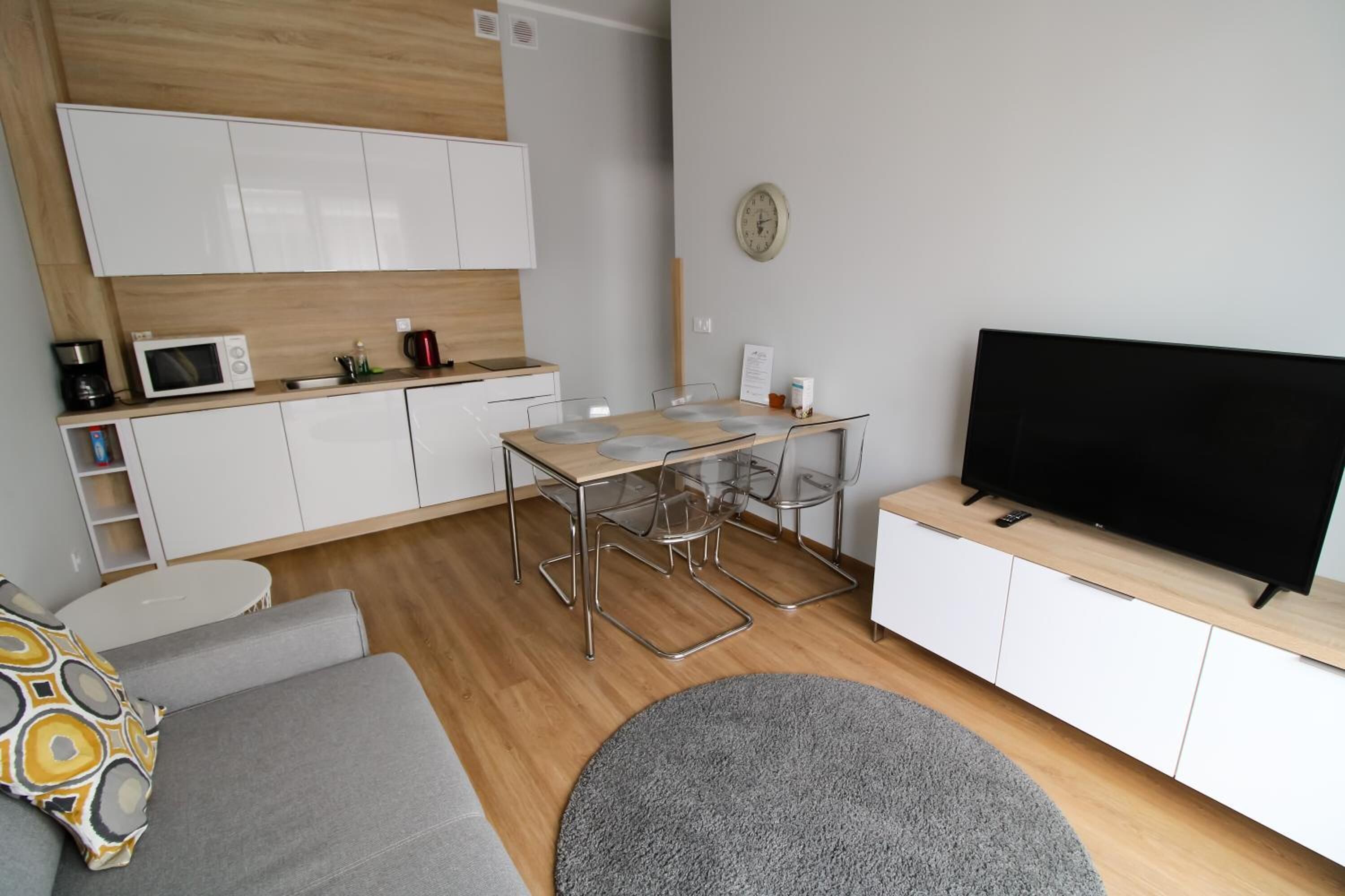 Una sala de estar moderna con un sofá, una mesa de comedor con sillas, un televisor de pantalla plana y una zona de cocina con armarios y electrodomésticos.