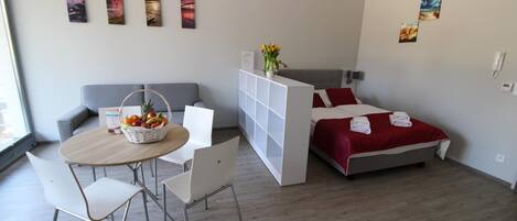 A modern hotel room with a bed, a seating area with a table and chairs, a small white cabinet, and artwork on the walls.