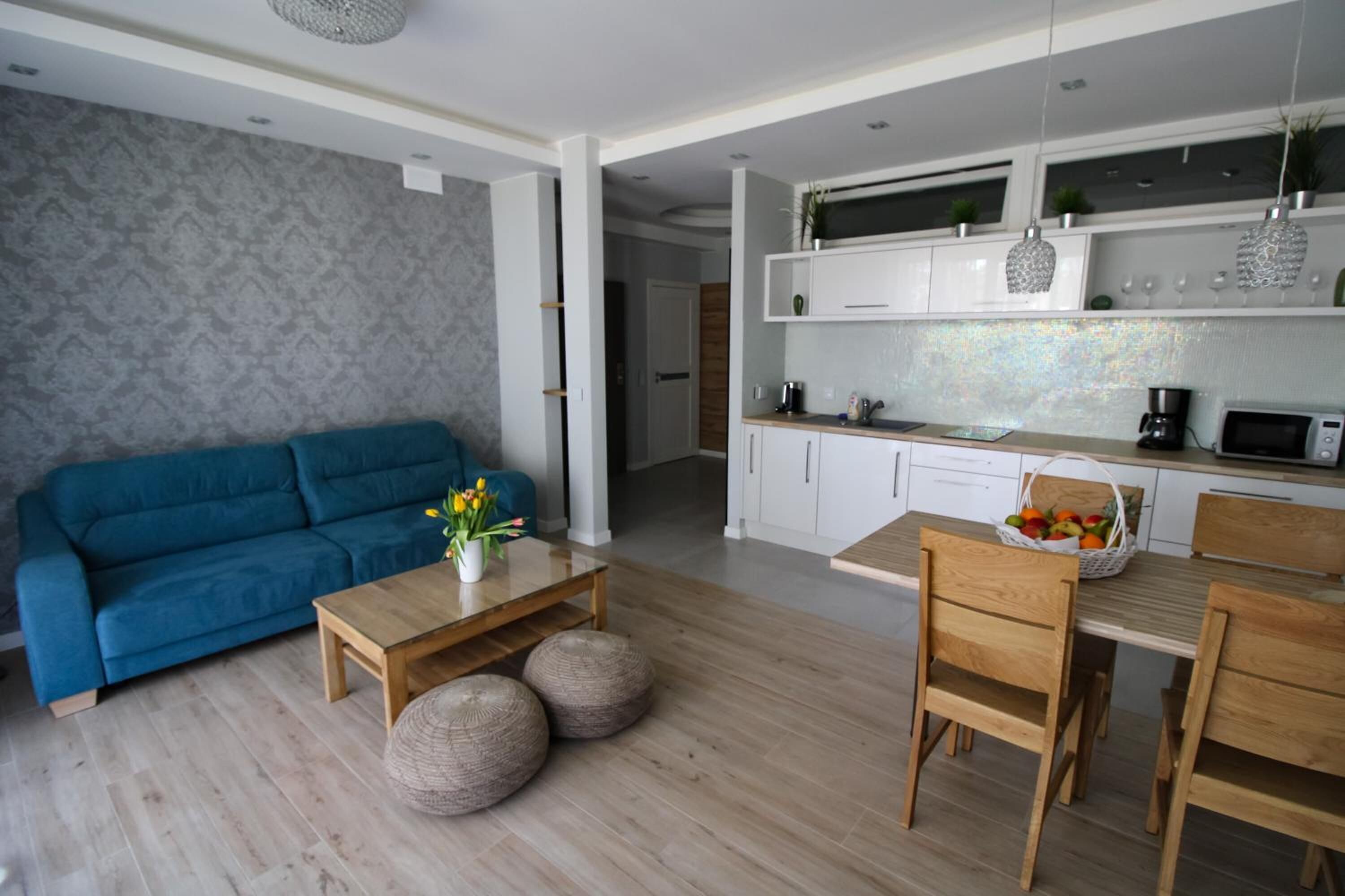 Una sala de estar moderna con un sofá azul, una mesa de centro de madera y un comedor con sillas y mesa de madera.