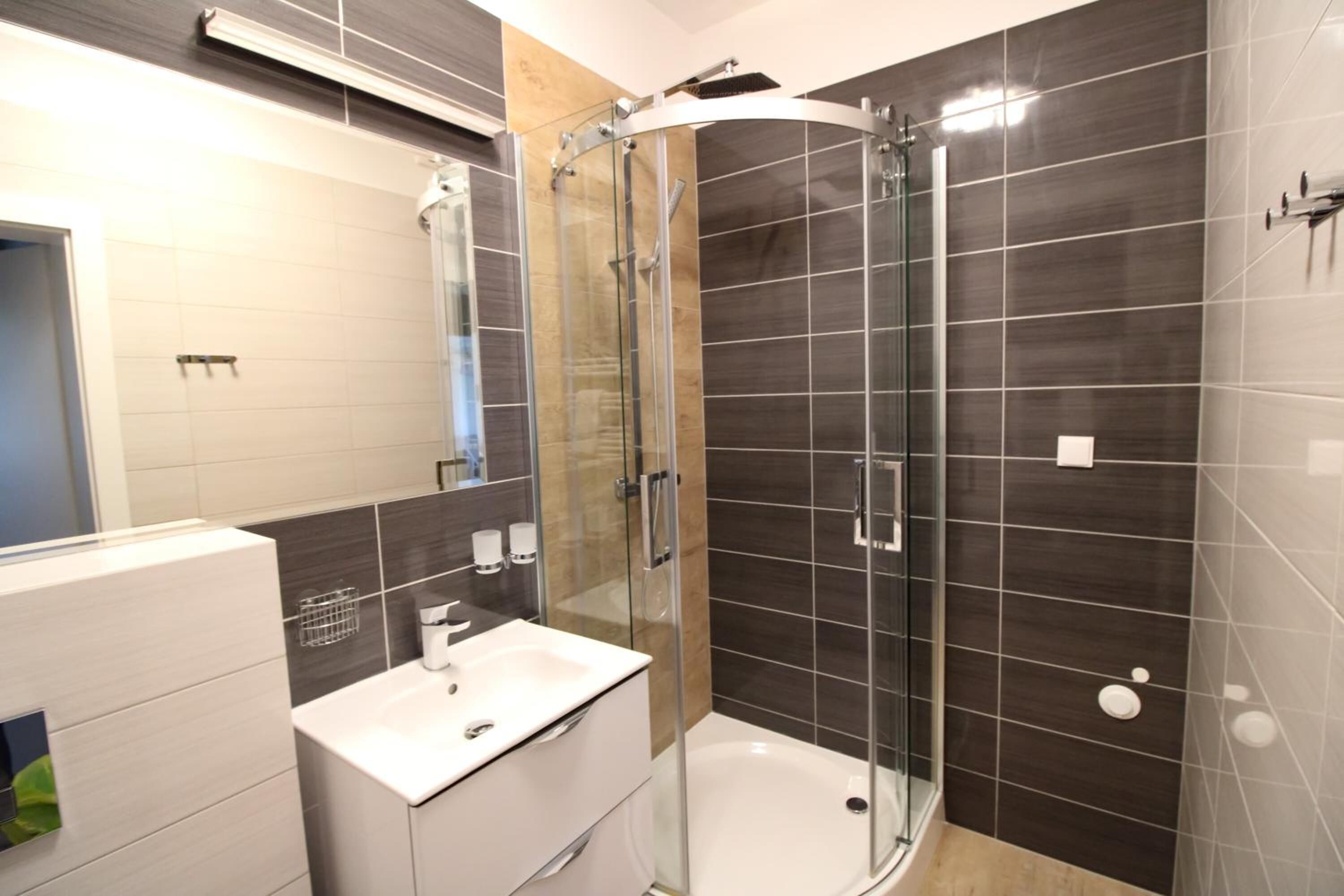 Un baño moderno con cabina de ducha de vidrio, lavabo blanco y paredes cubiertas de azulejos oscuros.