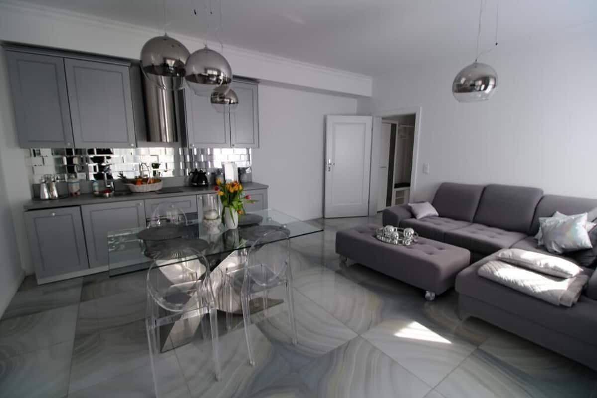 Eine moderne Küche mit grauen Schränken, einem Glastisch und einem grauen Sofa.