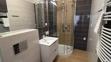 A modern bathroom with a glass-enclosed shower, a white sink, and a towel rack.