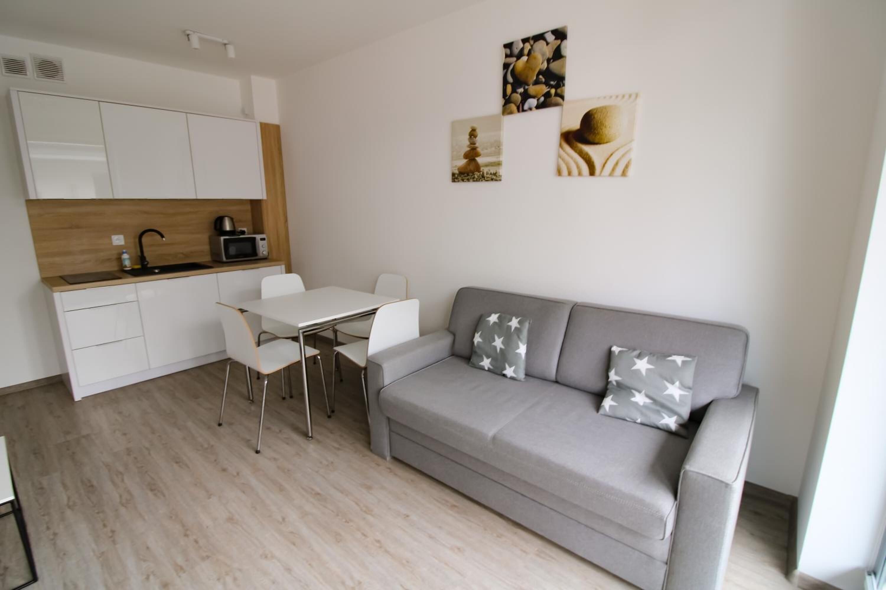 A modern living space with a grey sofa, white dining table, and chairs, a kitchenette, and artwork on the walls.