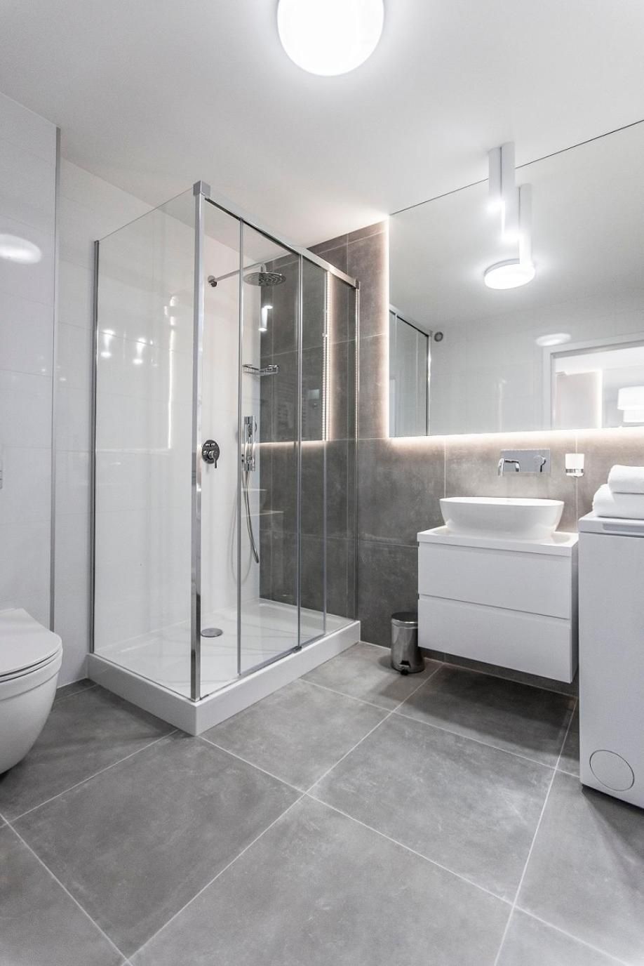 A modern bathroom with a glass-enclosed shower, a white sink, and a large mirror.