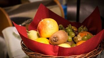 Una cesta de mimbre llena de frutas y verduras, como manzanas, kiwis y uvas, envueltas en papel rojo.