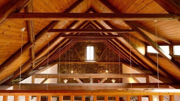 Estrutura de madeira com pé-direito alto, design de telhado triangular e claraboia central.