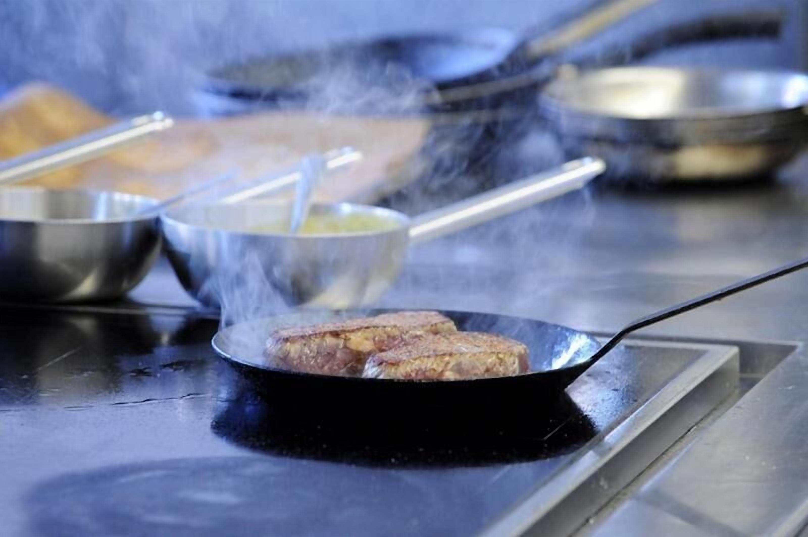 A cooking scene with a pan on a stove, steam rising, and various kitchen utensils and bowls in the background.