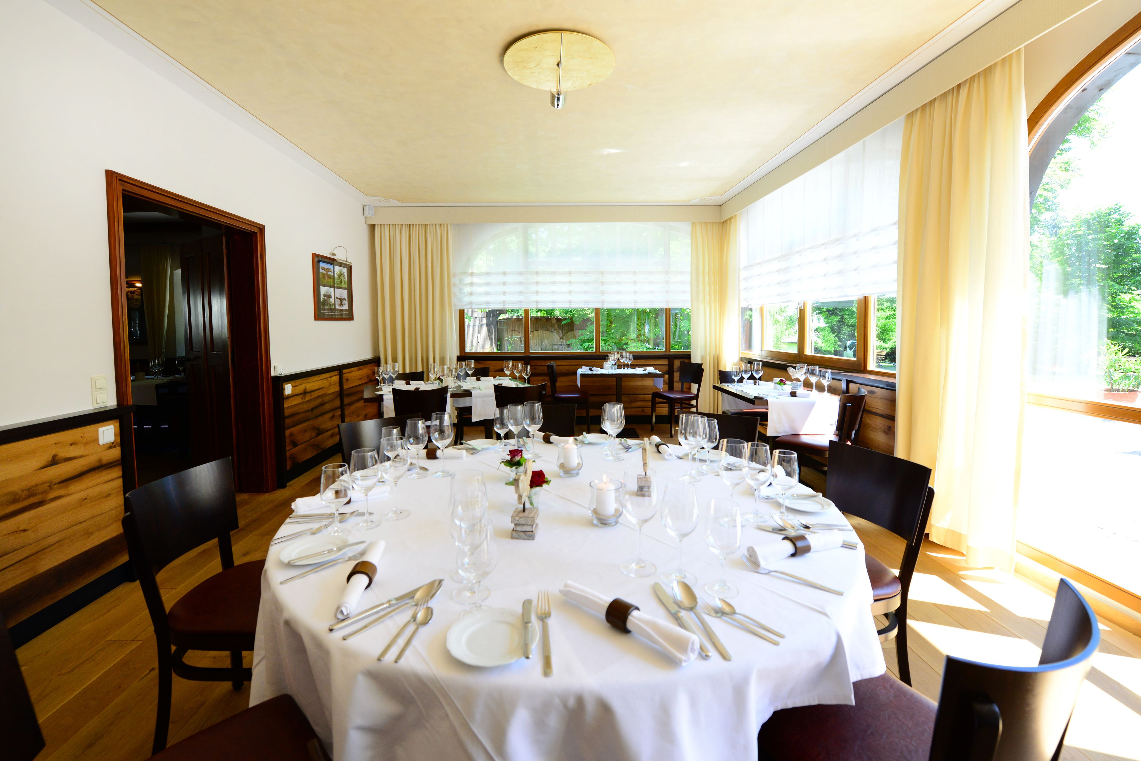A dining area with round tables set for a meal, featuring white tablecloths, neatly arranged cutlery, and wine glasses.