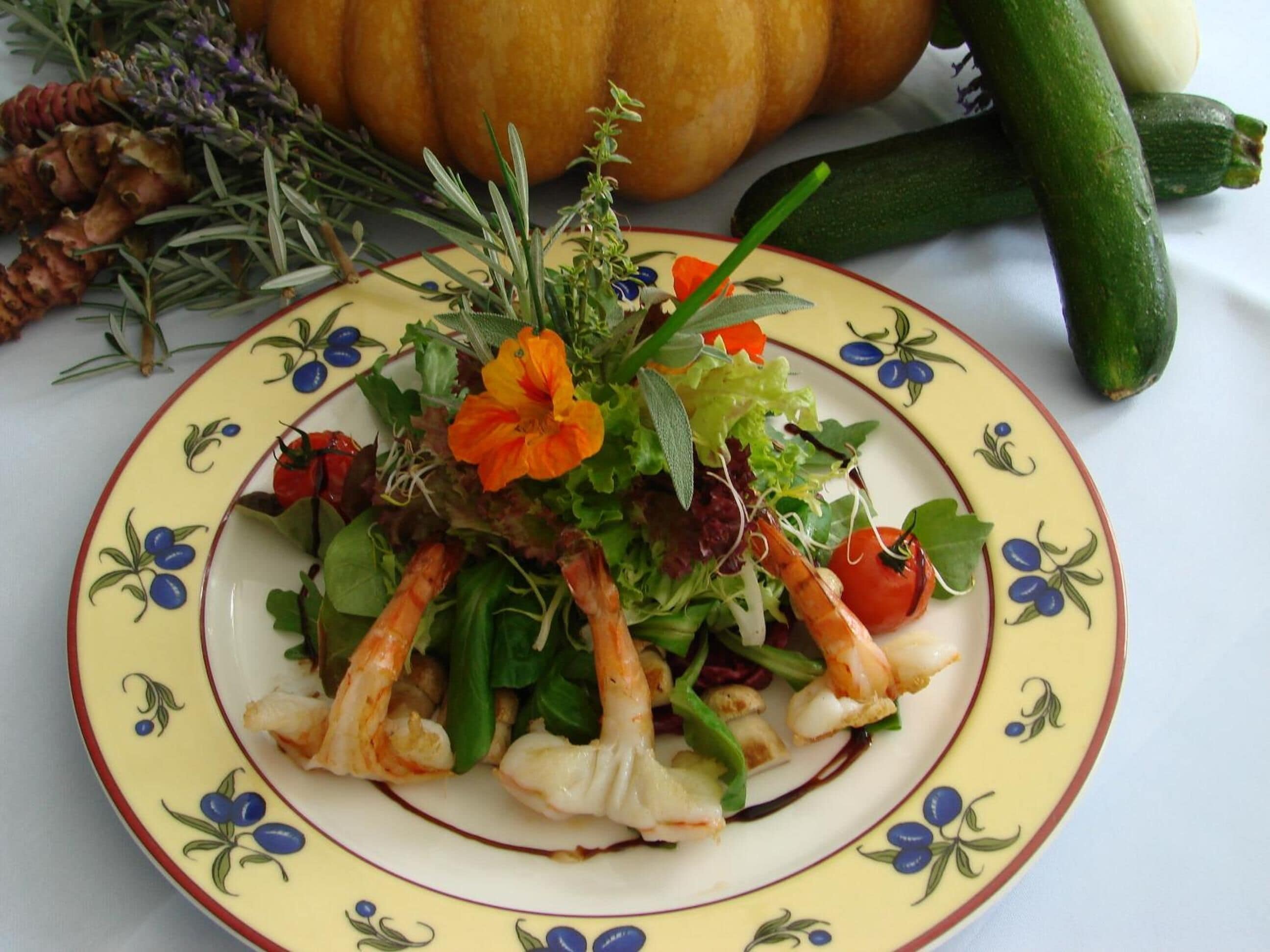 A plate of seafood salad with various vegetables and herbs, accompanied by a pumpkin and zucchini on the side.