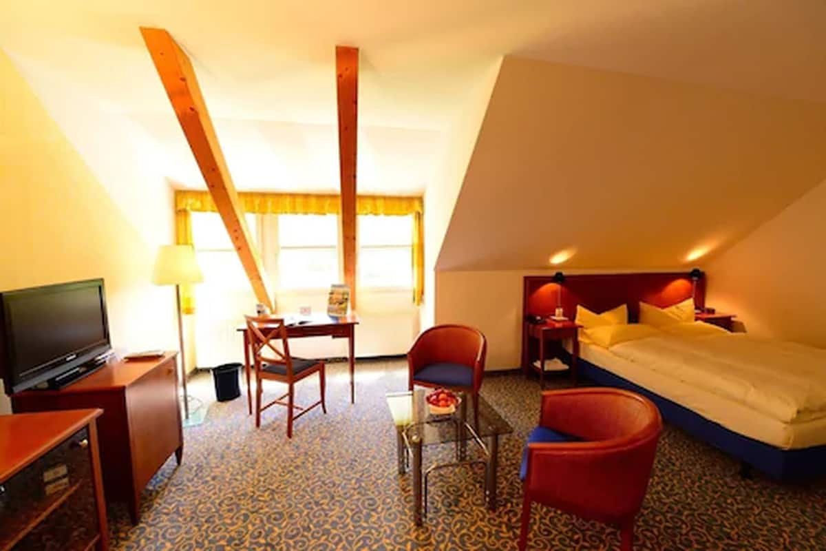 Habitación de hotel con cama, escritorio, silla, televisión y ventana con cortinas.