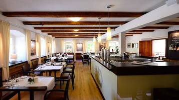 A restaurant with wooden beams, tables set for dining, and a bar area.