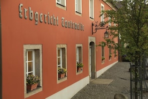A building with the sign "Erbgutrecht Coutellwölk" and multiple windows with flower boxes.