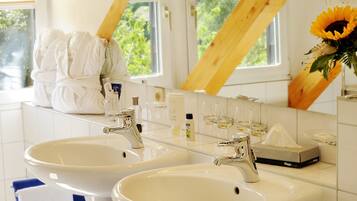 A bathroom with two sinks, a mirror, and a window with a view of greenery.