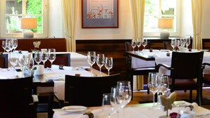 Restaurante com mesas preparadas para refeições, exibindo uma ilustração botânica emoldurada na parede e vista para o verde lá fora.