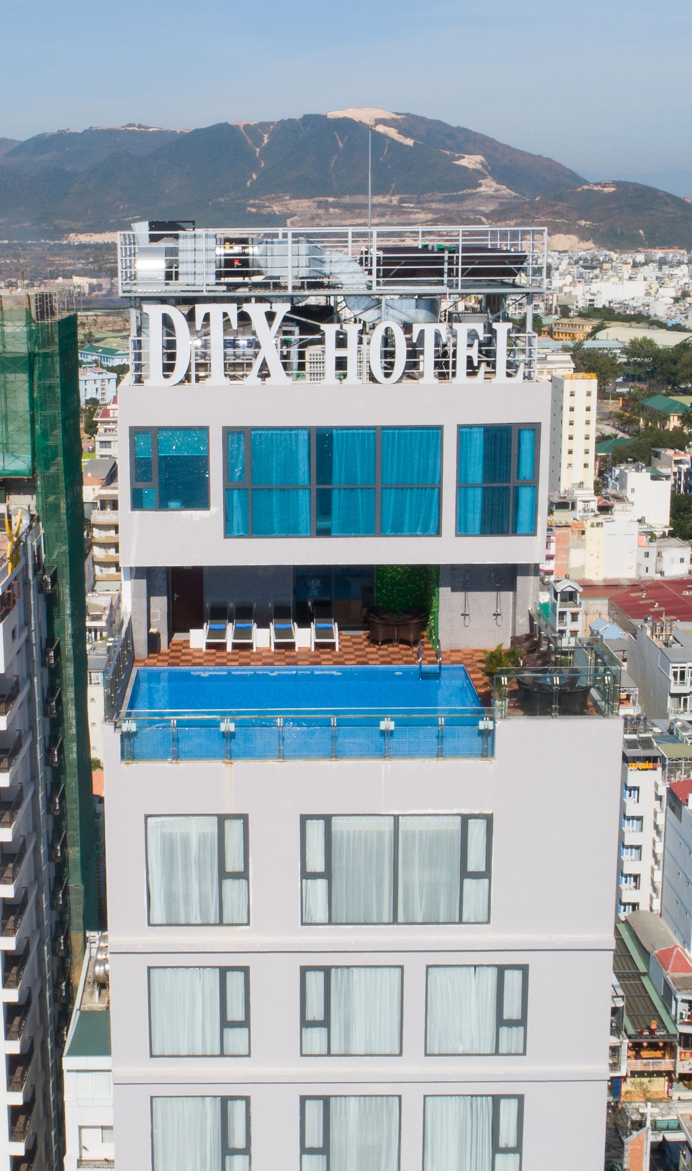 A hotel with a rooftop pool, large windows, and a view of the city and mountains in the background.