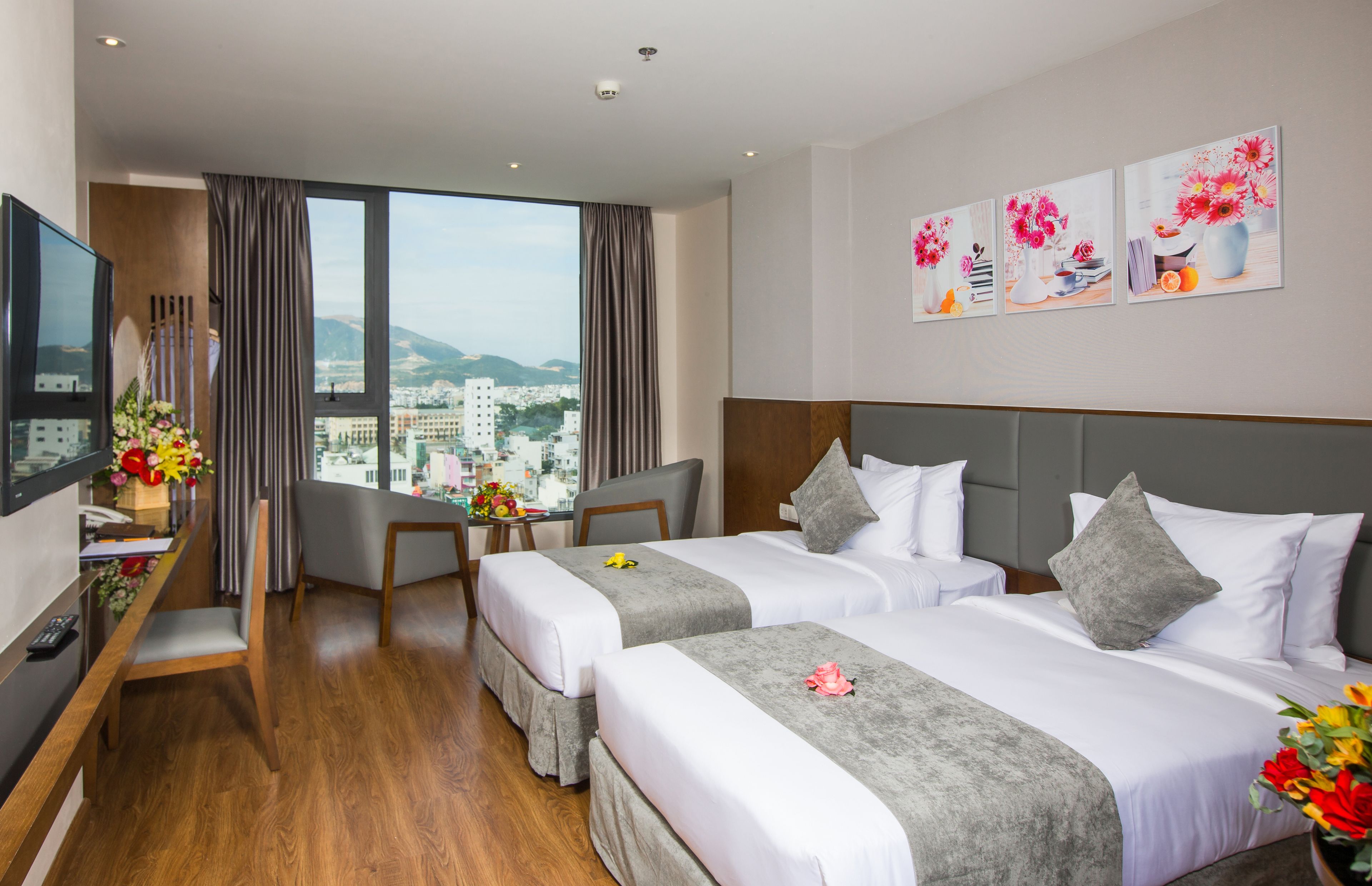 Ein Hotelzimmer mit zwei Betten, einem Schreibtisch, einem Fernseher und Blick auf die Stadt.