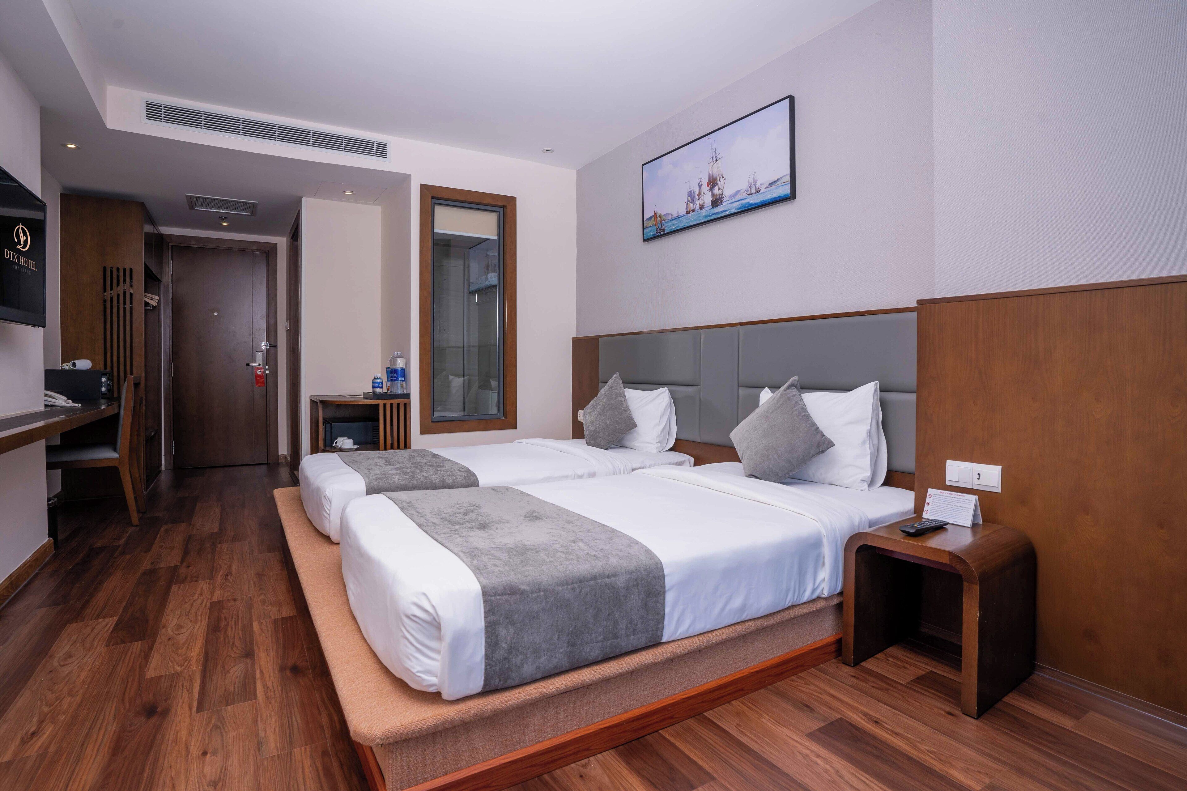 A hotel room with two beds, a desk, a chair, a small table, and a TV.