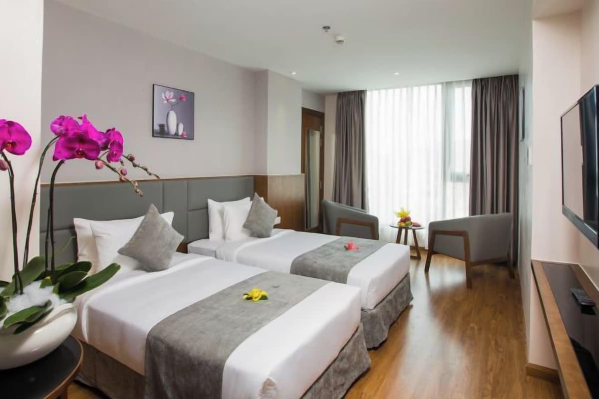 Een hotelkamer met twee bedden, een televisie, een bureau en een raam met gordijnen.