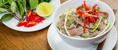Un tazón de sopa con carne y verduras, media lima y chiles rojos en un plato.