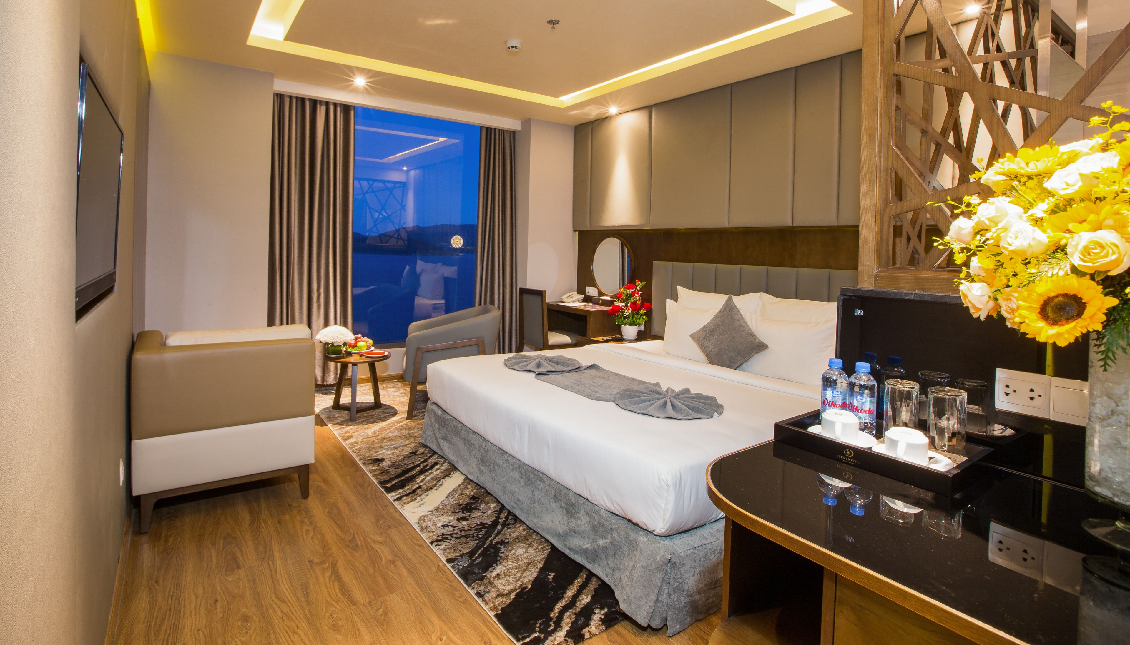 Habitación de hotel moderna con una cama grande, un escritorio, un sofá y vistas a la ciudad de noche.