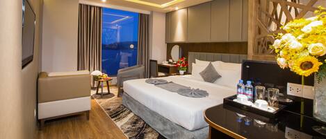 Habitación de hotel moderna con una cama grande, un escritorio, un sofá y vistas a la ciudad de noche.