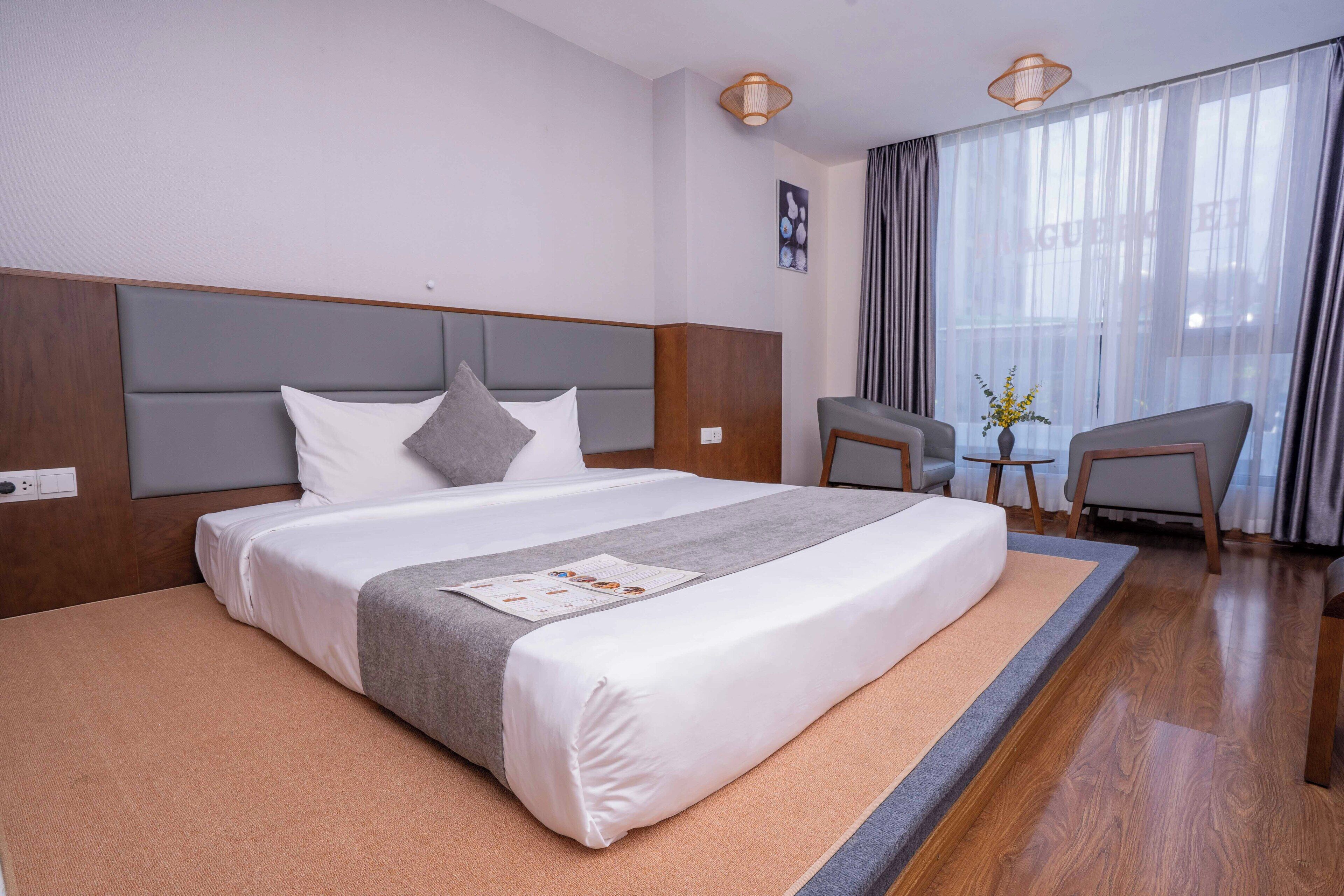 Een hotelkamer met een groot bed, een houten hoofdbord, een bijzettafeltje met een vaas en een stoel.