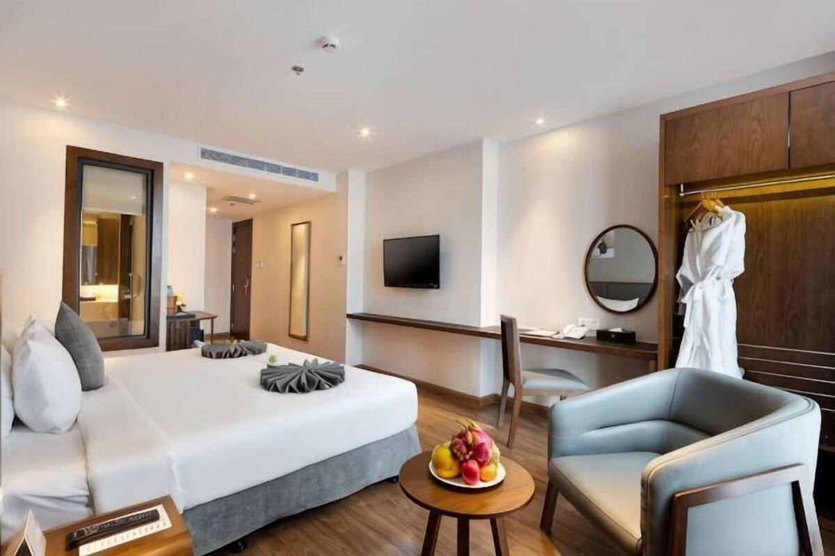 Ein Hotelzimmer mit Bett, Schreibtisch, Stuhl, Fernseher, Spiegel und Kleiderhaken.
