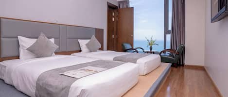 A hotel room with two beds, a wooden headboard, a large window with curtains, a TV, and a seating area with a chair and a table.