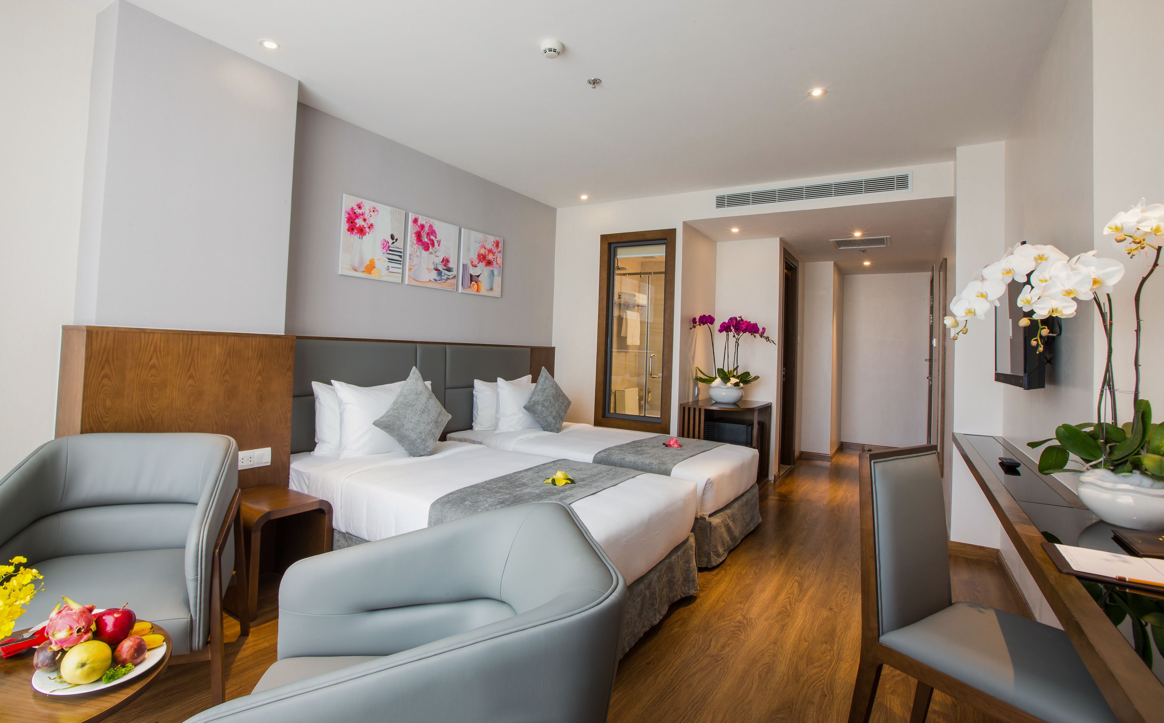 Ein Hotelzimmer mit Bett, zwei Sesseln, einem Schreibtisch und einem Esstisch. Ein Badezimmer ist durch eine Glastür sichtbar.