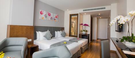 Ein Hotelzimmer mit Bett, zwei Sesseln, einem Schreibtisch und einem Esstisch. Ein Badezimmer ist durch eine Glastür sichtbar.