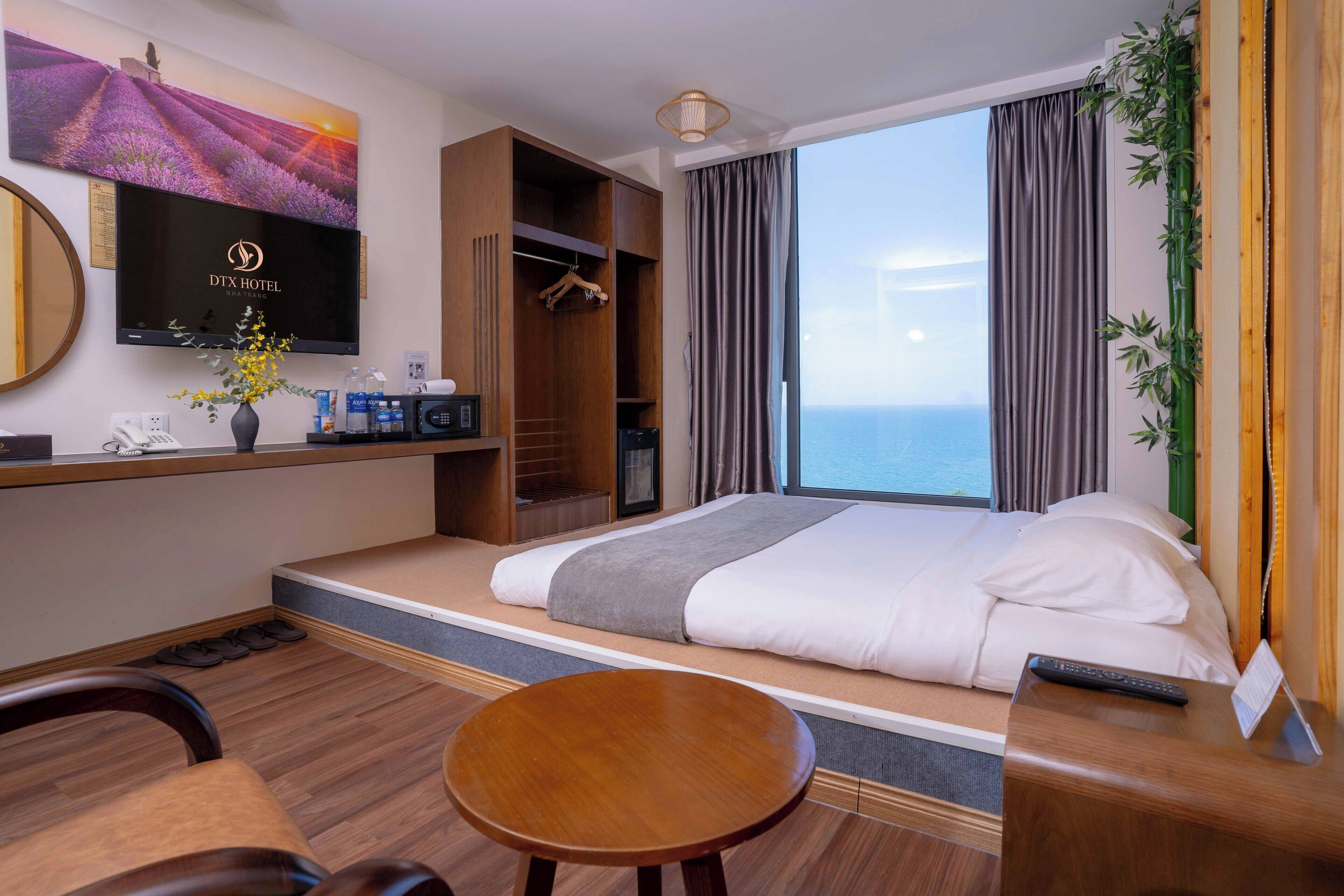 A hotel room with a bed, a desk, a TV, a wardrobe, and a view of the sea.