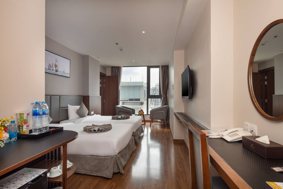 Ein Hotelzimmer mit einem großen Bett, einem Schreibtisch mit Telefon, einem Spiegel und einem Fenster mit Blick auf die Stadt.