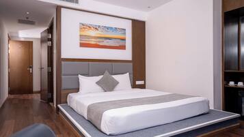 Habitación de hotel moderna con una cama grande, cabecera con estante integrado, un cuadro de un atardecer y suelo de madera.