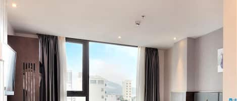 Habitación de hotel moderna con una cama grande, un escritorio y una silla. Se ve la ciudad a través de amplias ventanas.