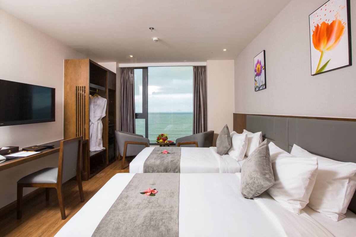 Ein Hotelzimmer mit zwei Betten, einem Schreibtisch, einem Fernseher und Blick aufs Meer.