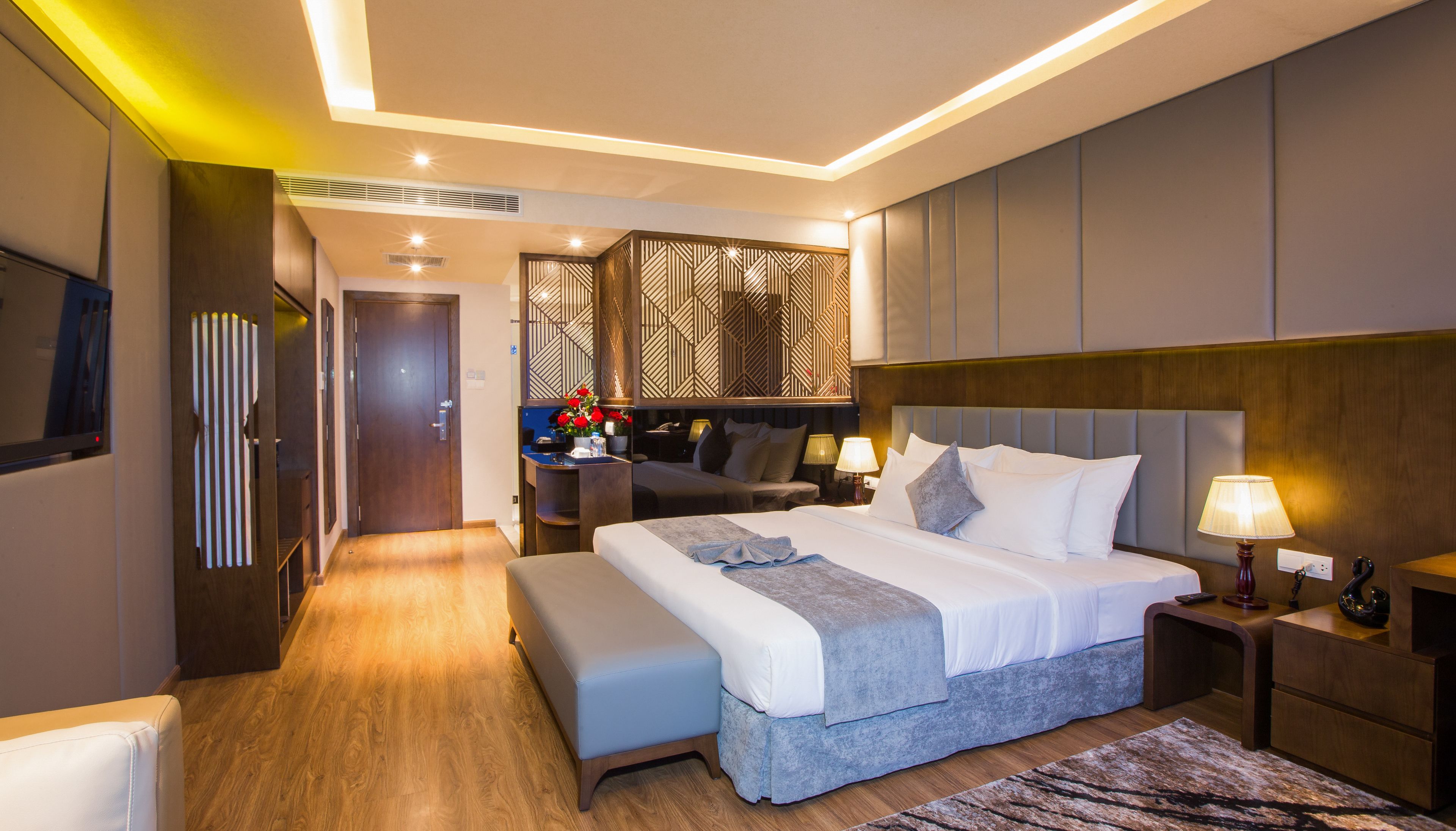 A modern hotel room with a large bed, bedside tables, a TV, and a decorative wall panel.