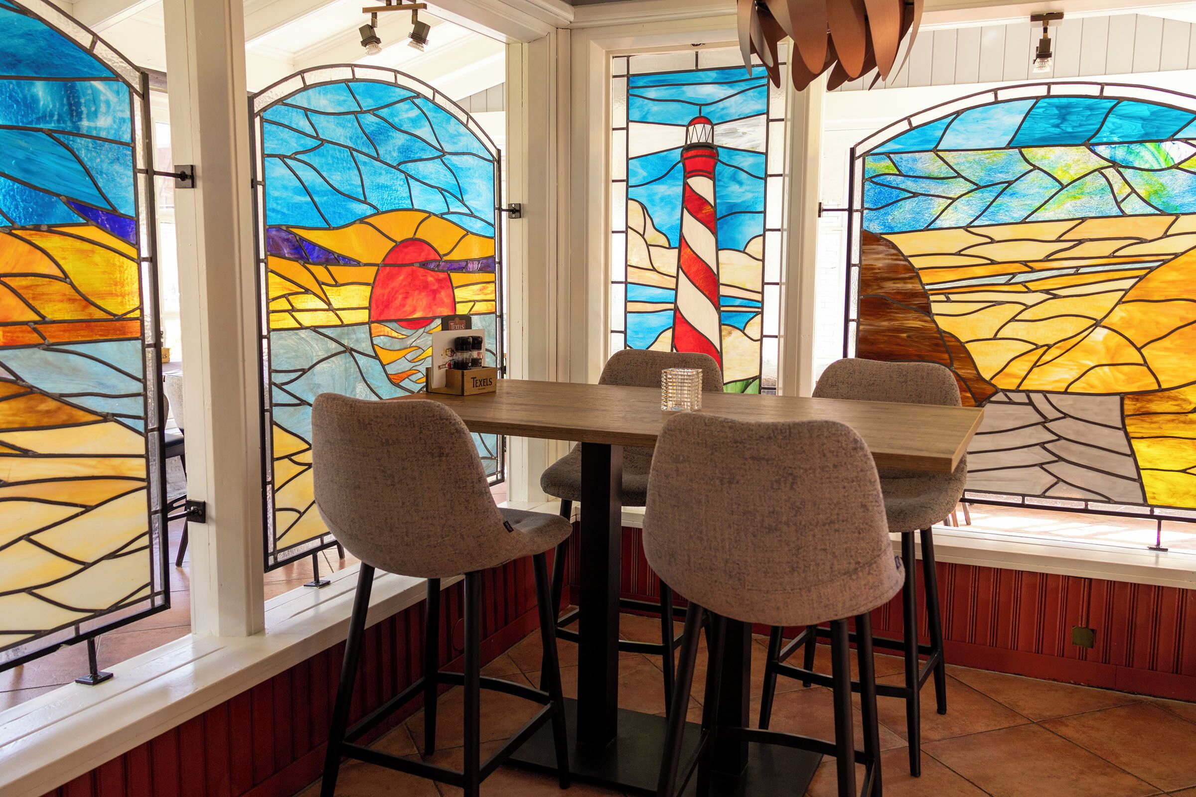A restaurant with a stained glass window featuring a lighthouse design, a wooden table, and four chairs.